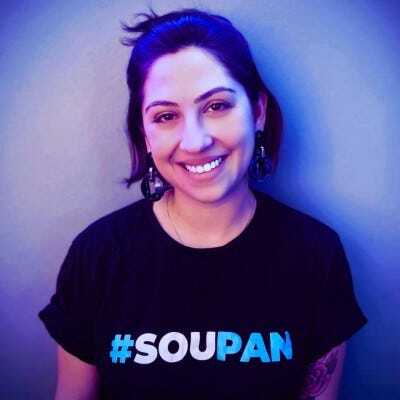 Mulher branca de cabelo escuro e curto sorrindo, com camisa preta com os dizeres